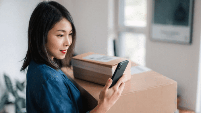 Woman looking at her mobile phone as she's carrying the packages for the delivery