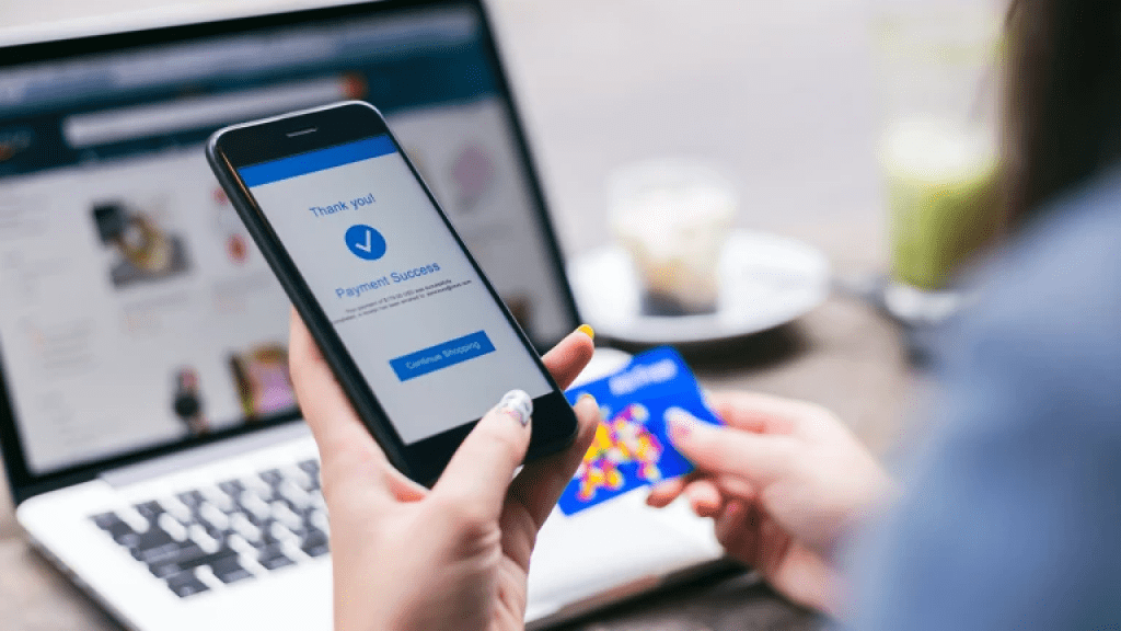 Close up of a hand holding a smartphone in one hand and a credit card in the other. On-screen text reads: Thank you! Payment Successful.